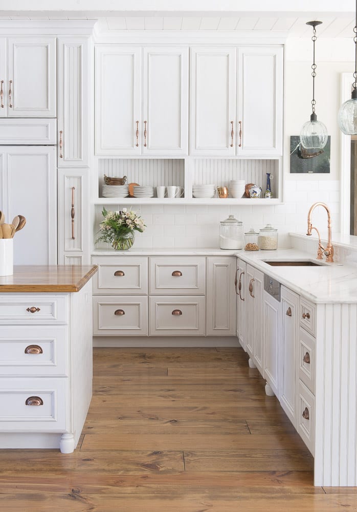 white kitchen with copper accents and wide wood plank floor