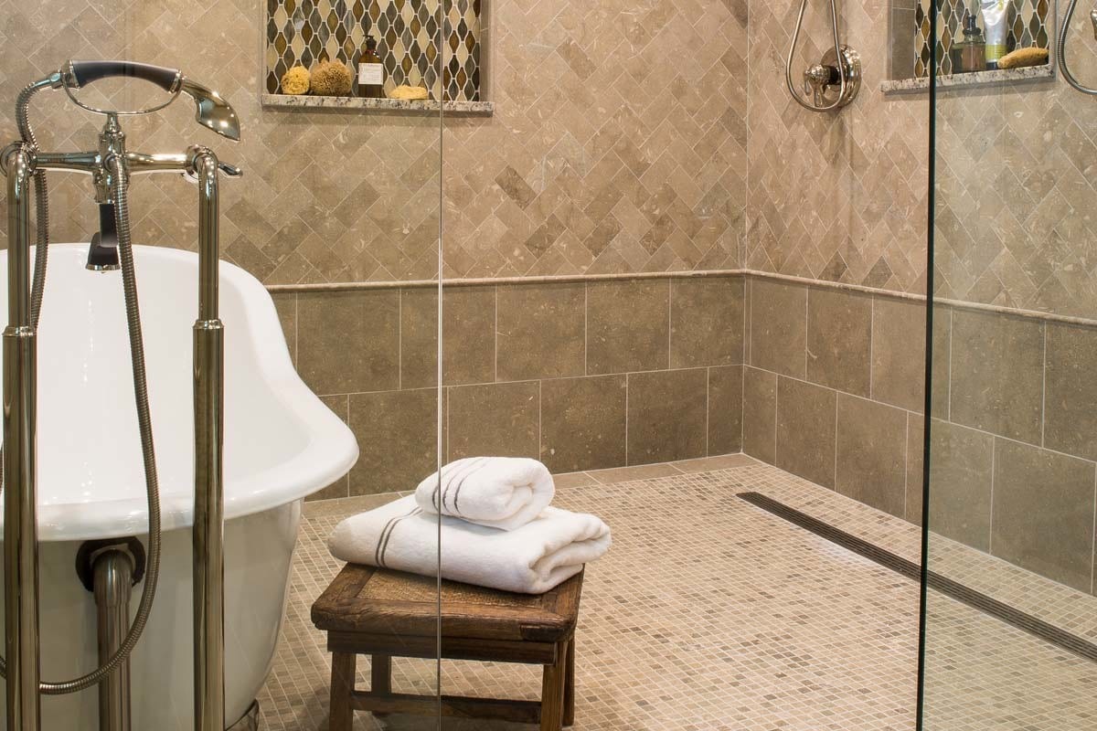a neutral tiled wet room with a freestanding white bathtub