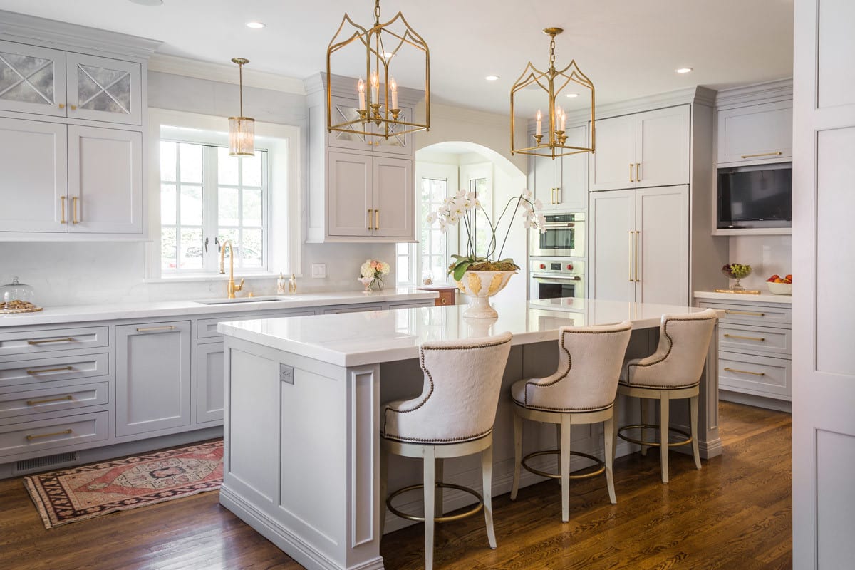 A spacious and bright kitchen remodel with light grey cabinetry, white countertops, and gold fixtures