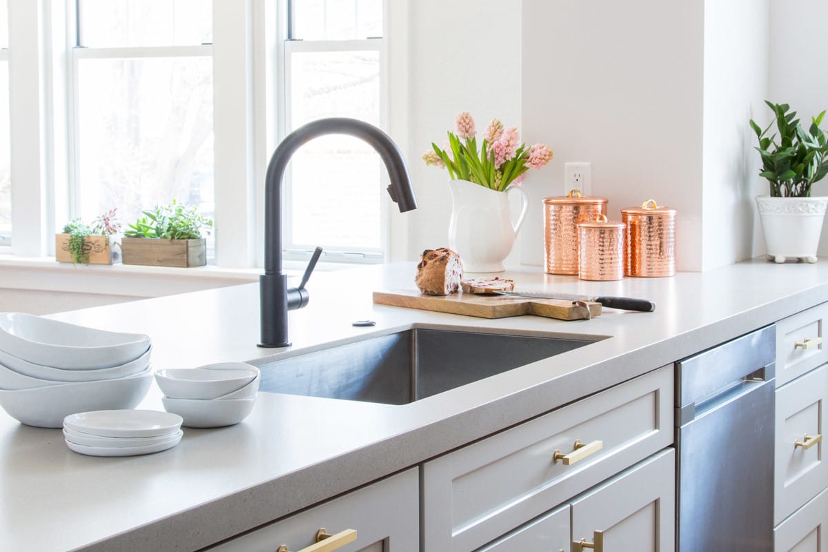 close up of a large grey kitchen island with a deep farm sink and black faucet