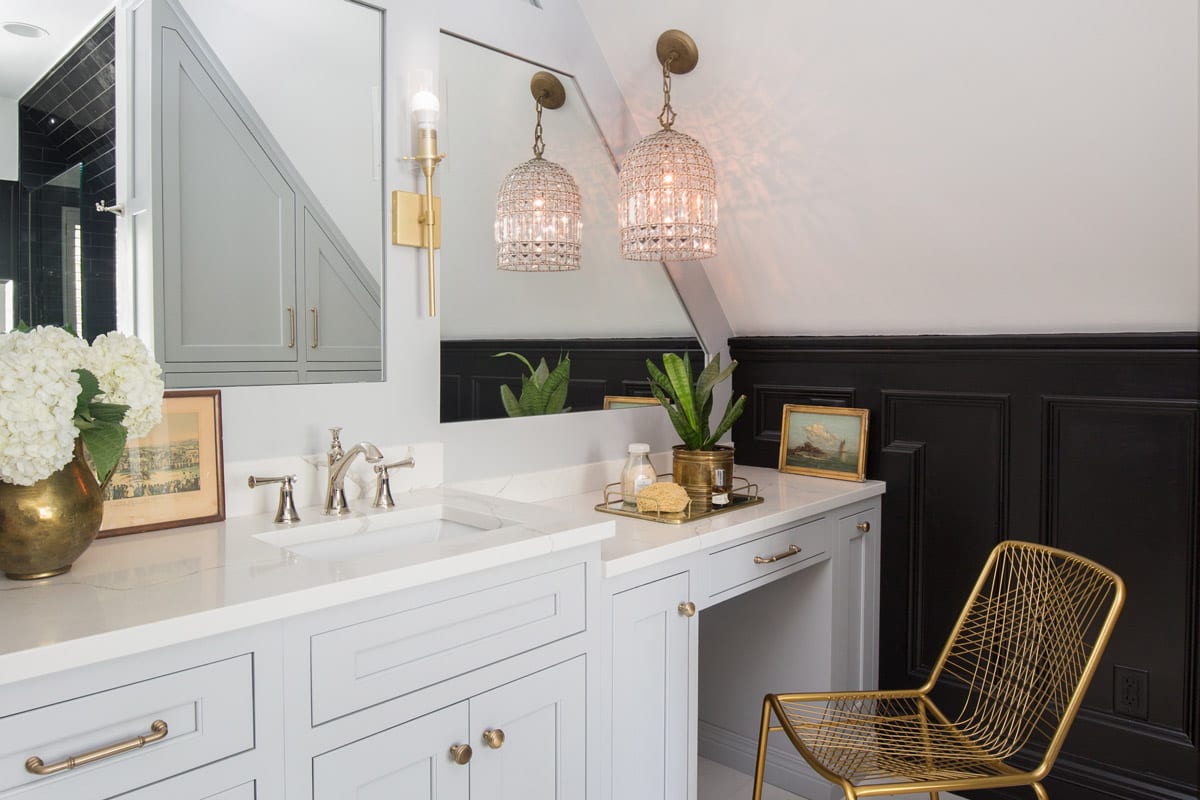 Newly renovated black and white bathroom countertop area with gold furniture, flowerpots, and light fixtures.