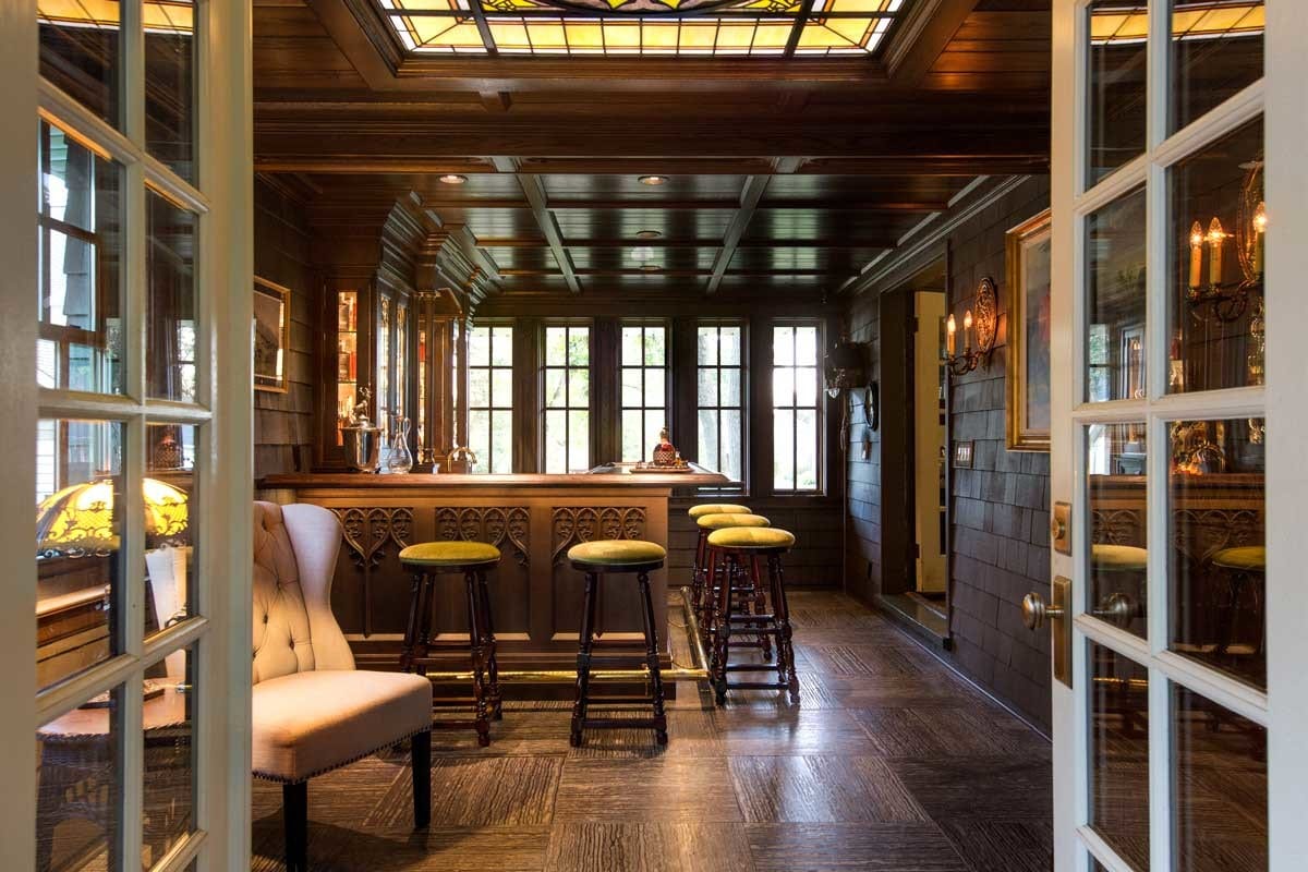 This is not your typical basement bar. It’s nestled into the front porch, stealing its long length from a little more than half of the old screened in area. There are original glass French doors that lead directly to the formal dining room. Light comes from all sides, yet the mood is dark. The beam ceiling was created from a dying white oak that stood in the front yard for 180 years, long before the historic home was built.