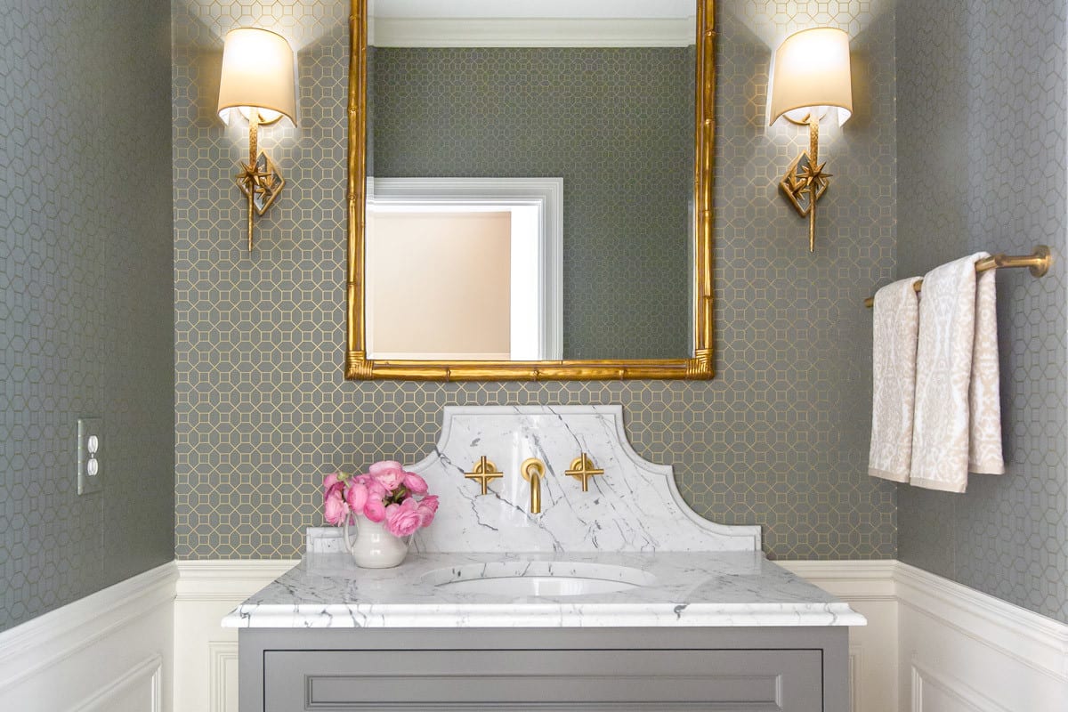 grey white gold bathroom interior design. granite countertop over grey cabinets with pink flowers and gold lights on walls.