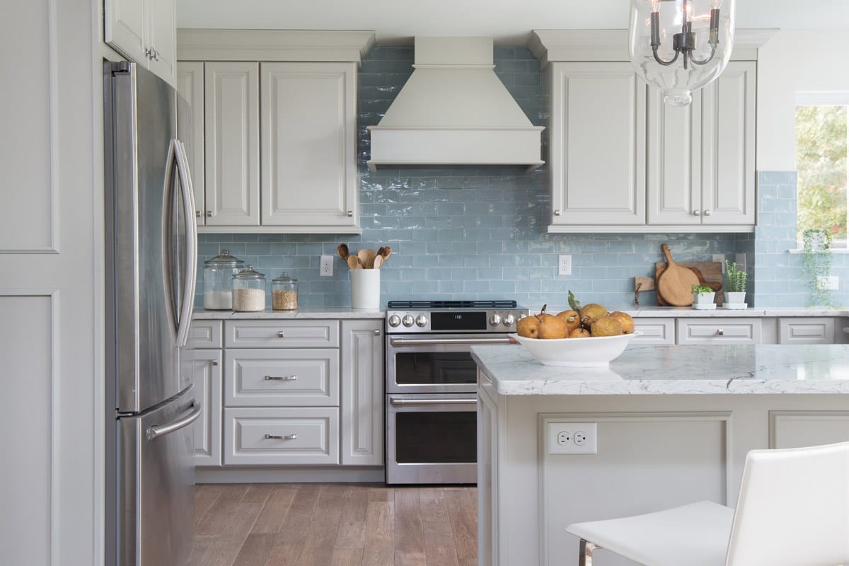 a large airy kitchen with glossy blue backsplash and white cabinetry