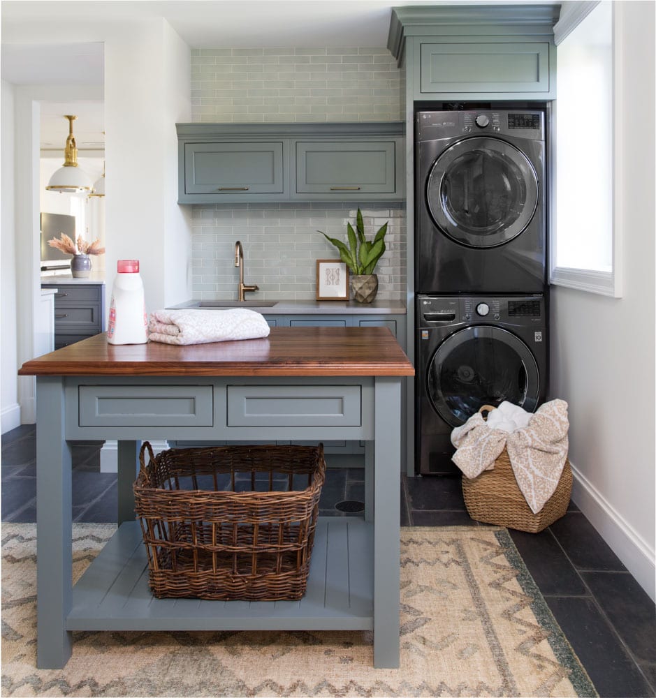 A white and dusty-blue-colored laundry room with cabinet space to store laundry products and baskets.