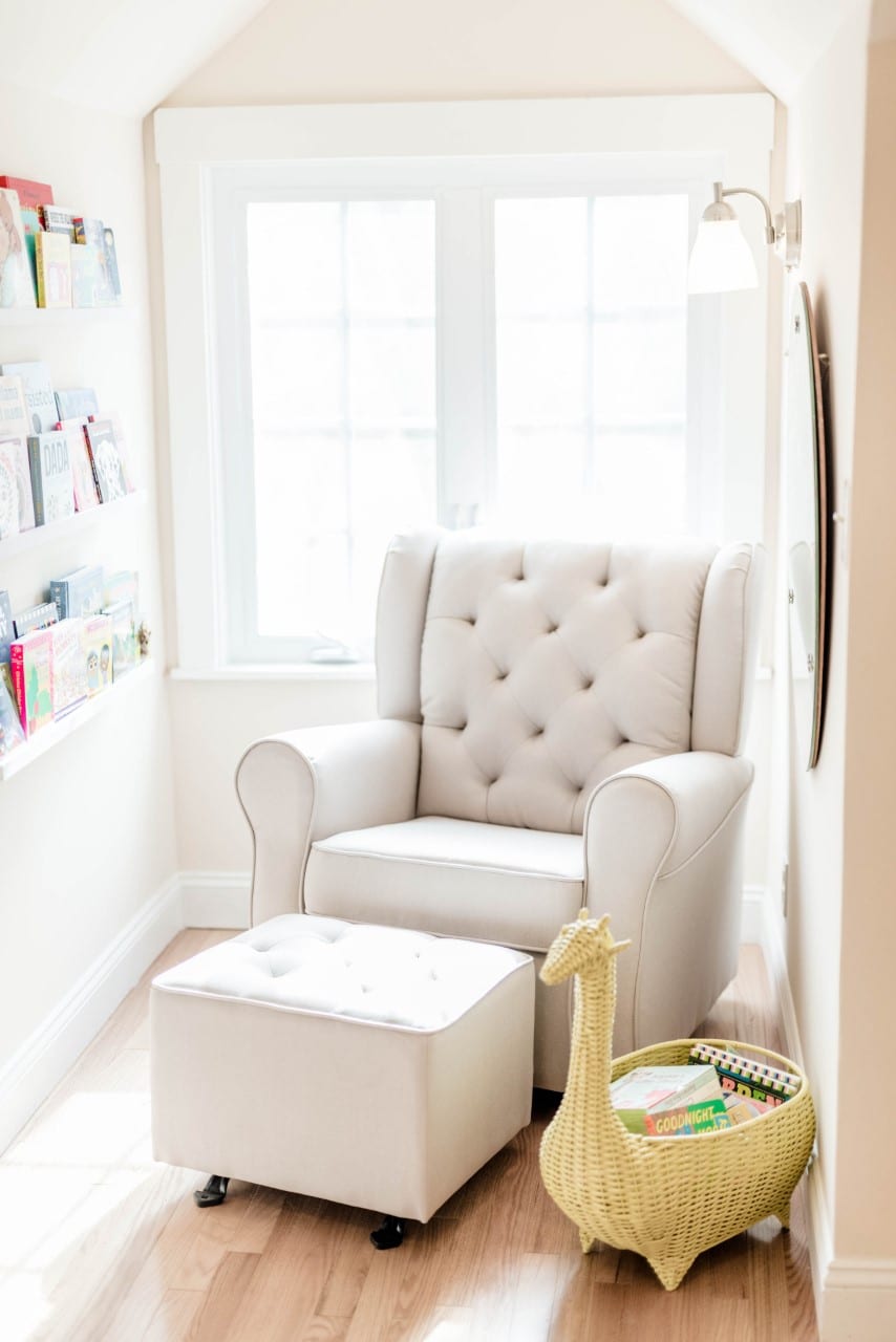 A chair sits in a nook in a room, with bookshelves filled with children's books and a large window for natural light.