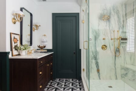 A primarily black and white bathroom with golden accents and light fixtures. There is a large black vanity next to a glass-enclosed shower.