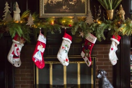 A fireplace adorned with Christmas decorations including stockings, foliage, and lights.