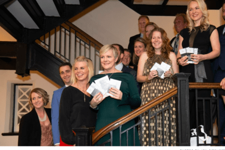 A group of sharply-dressed individuals hold cards and pieces of paper while standing on a staircase.