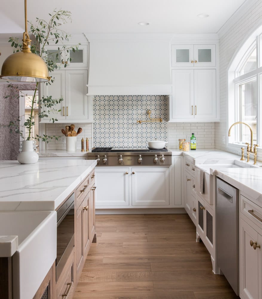 A long kitchen remodel with white and wooden cabinets along with golden accents and a black and white patterned backsplash.