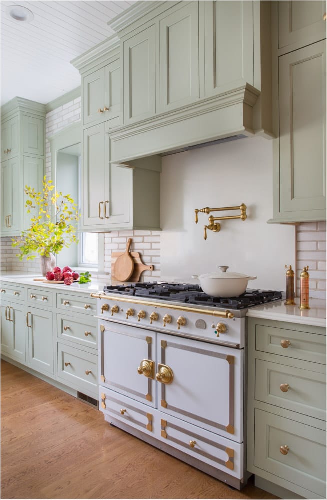 Pastel green cabinets with gold accents and white brick backsplash in a cute pastel themed kitchen.
