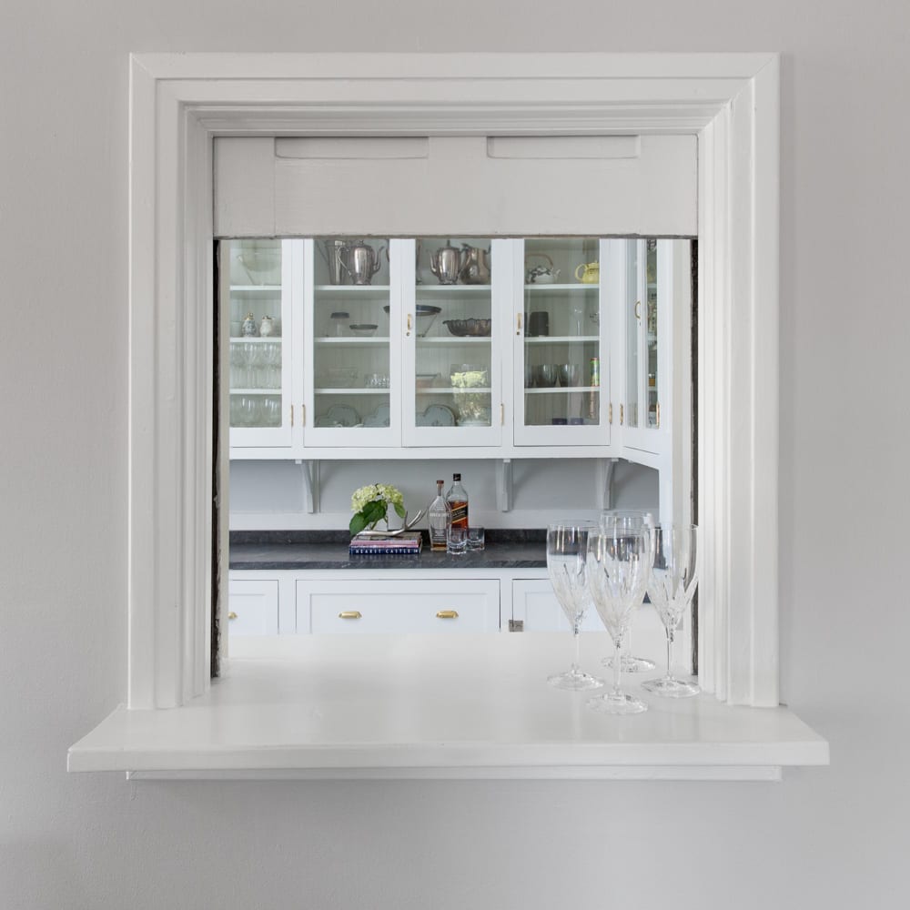view of a white kitchen interior design through a white window with wine glasses sitting on the windowsill.