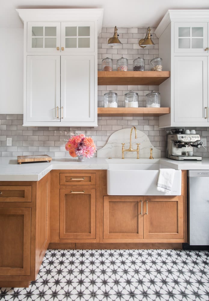 White and wooden cabinets in a kitchen with black and white tiled flooring and a grey brick backsplash.