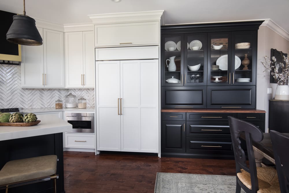 Kitchen has both black and white cabinets. The fridge is built into white cabinets