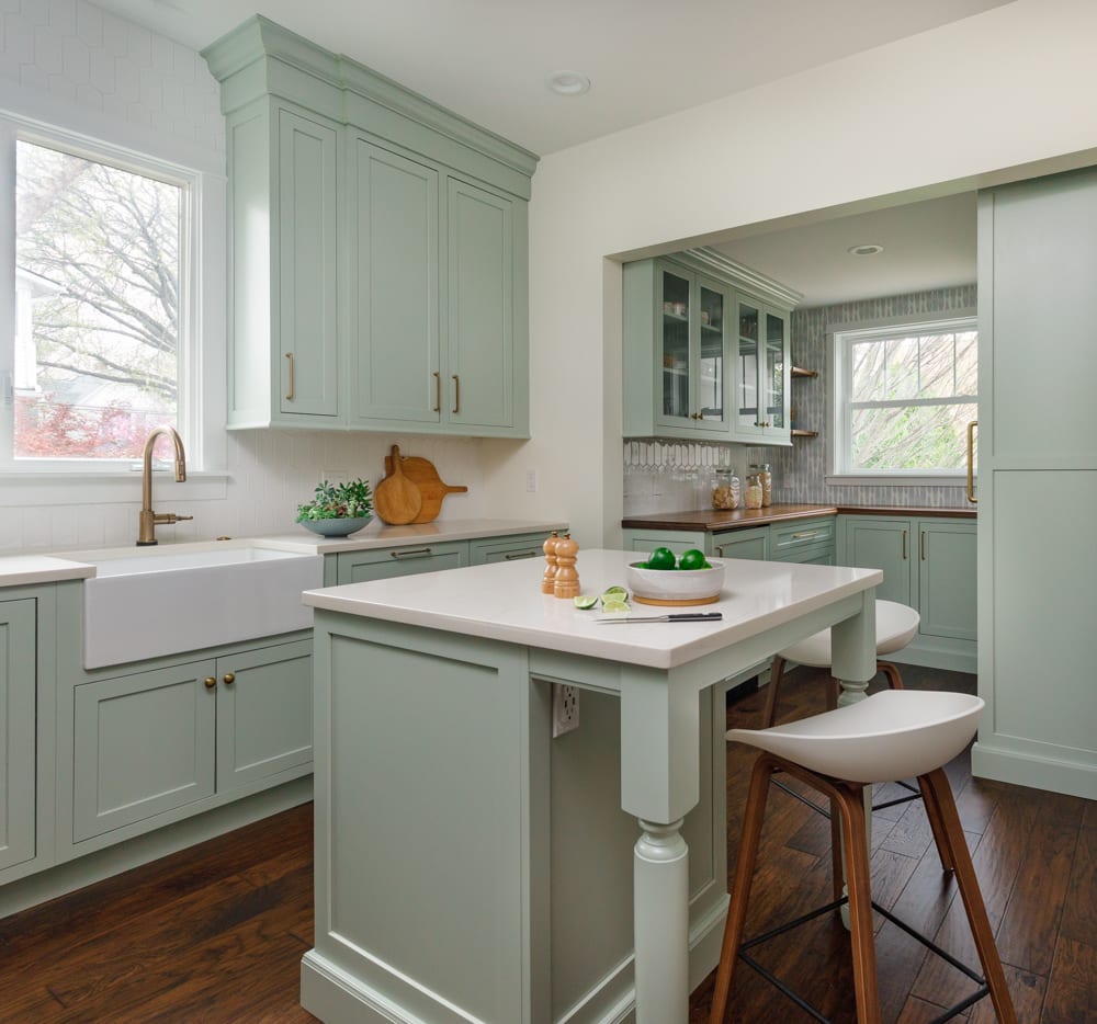 The cabinets are sage green with gold hardware and the countertops are white