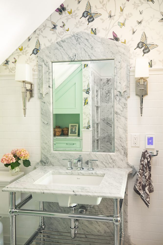 marble vanity and mirror in a bathroom with silver hardware and butterfly wallpaper