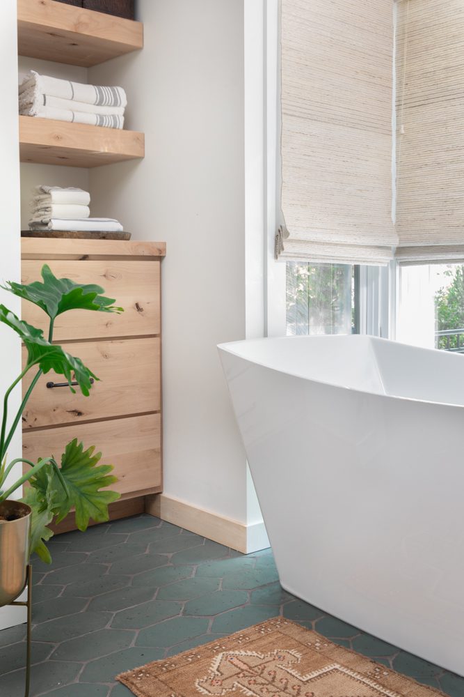 freestanding bathtub in bathroom next to large windows letting light in