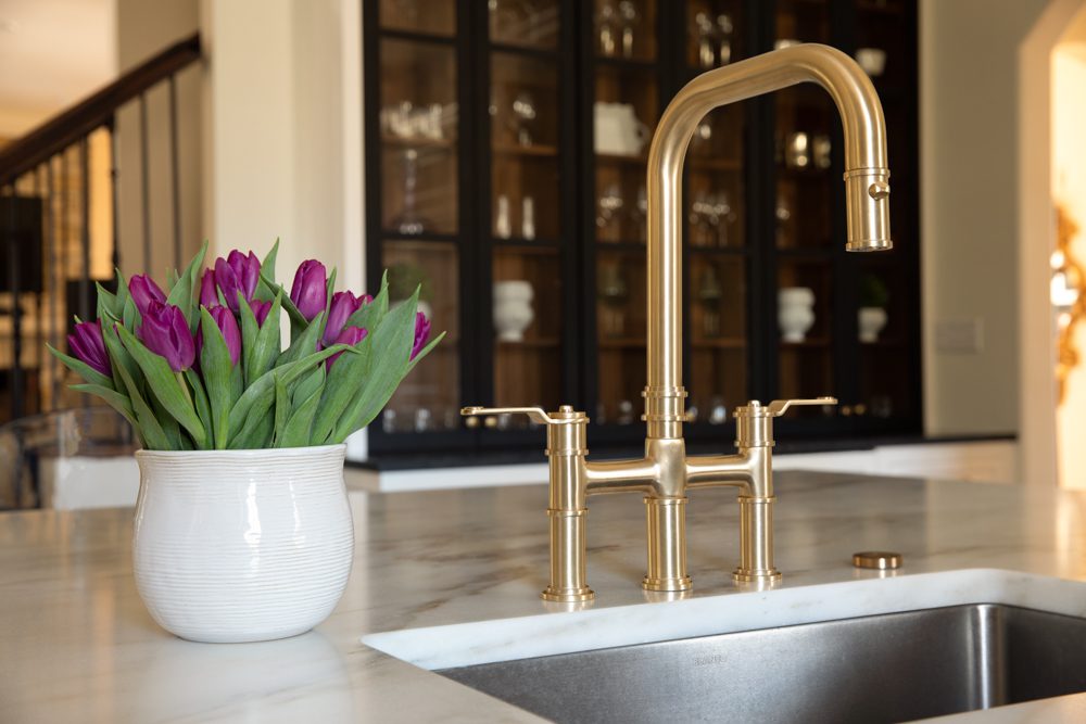 large steel sink with gold faucet and marble countertops