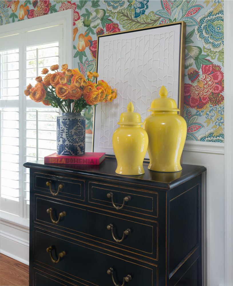 a dresser in a room with bright decor and floral wallpaper
