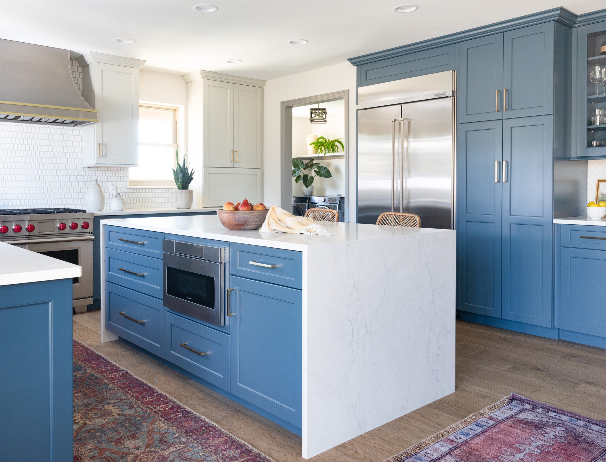 a marble waterfall island and blue cabinets really make this kitchen pop!