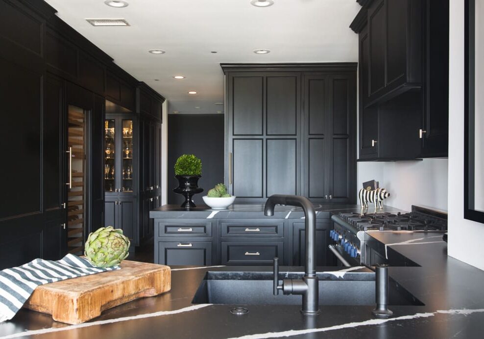 Carondolet-146-Edit Black kitchen with white ceilings and walls with silver handles and accents and a wooden cutting board next to the sink.