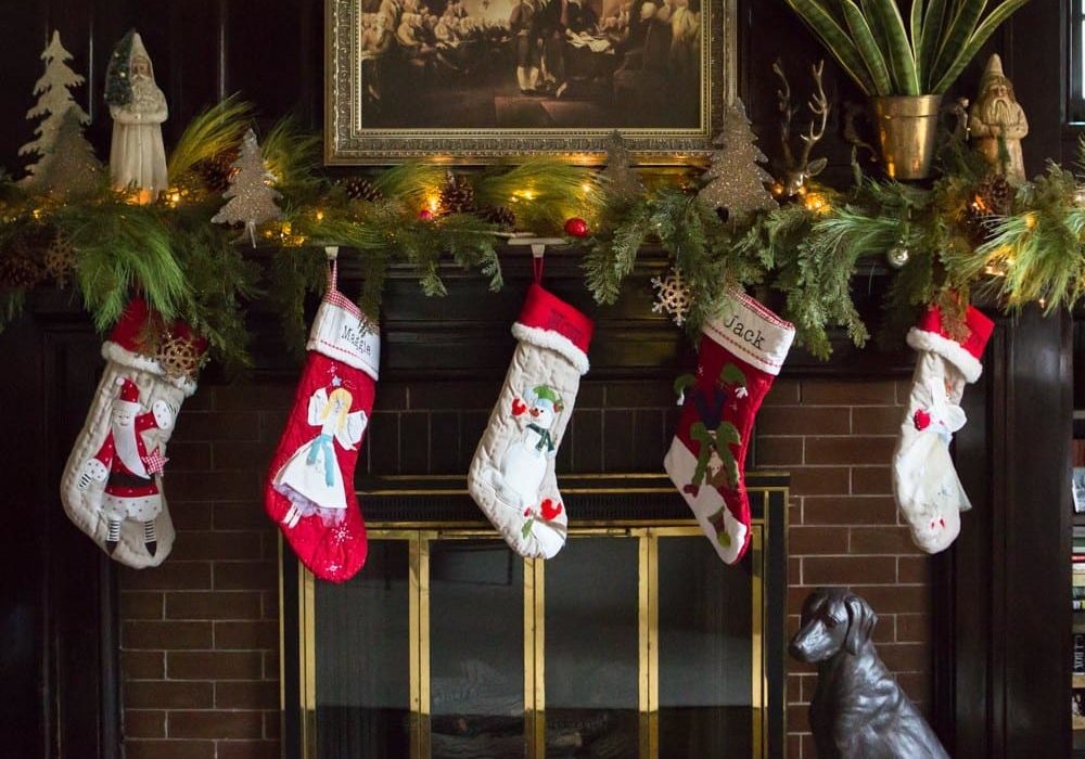 A fireplace adorned with Christmas decorations including stockings, foliage, and lights.