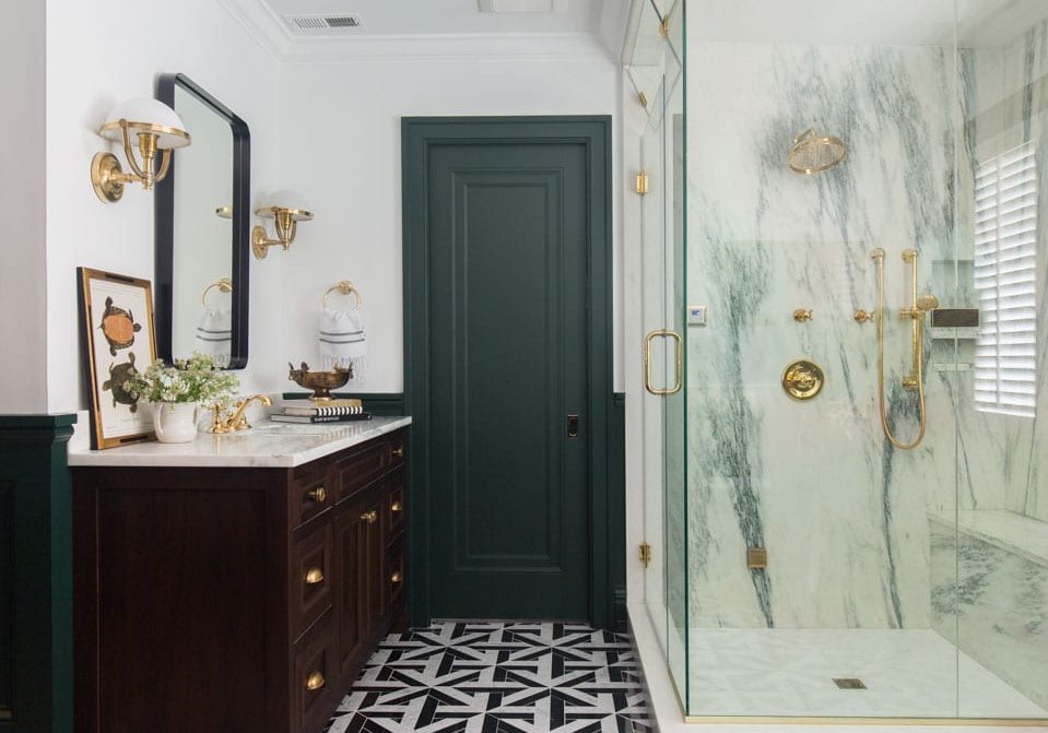 A primarily black and white bathroom with golden accents and light fixtures. There is a large black vanity next to a glass-enclosed shower.