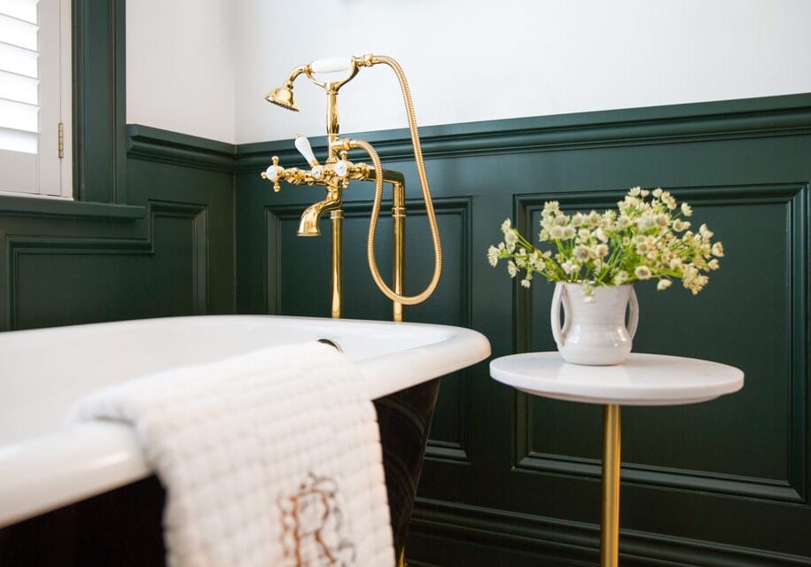 Sherwood Dr II-316200928-Edit A white flowered plant sits atop a small table next to a bathtub in a black and white bathroom with gold accents.
